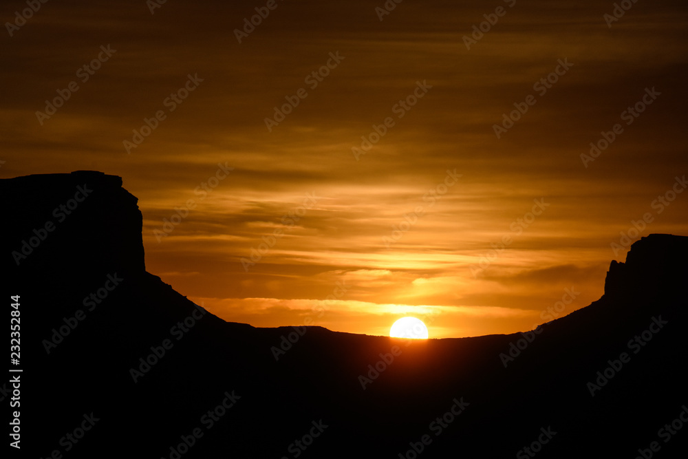 Silhouette of the famous rock formations in Monument Valley on the Utah Arizona border at sunrise with a bright orange sky.