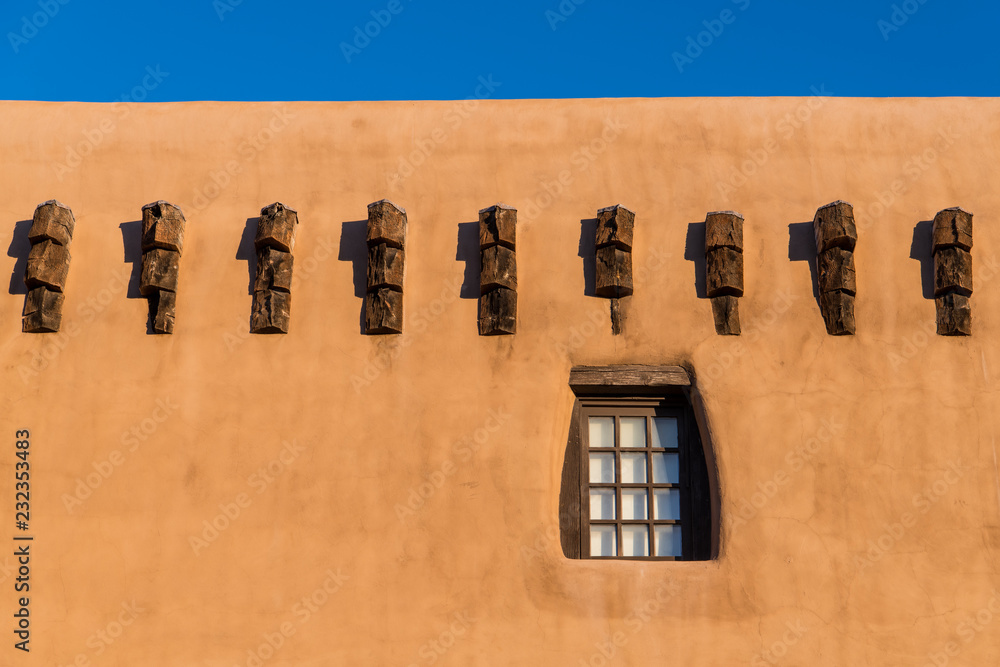 Naklejka premium Pueblo style adobe building wall and rustic wood-framed window and beam ends in Santa Fe, New Mexico