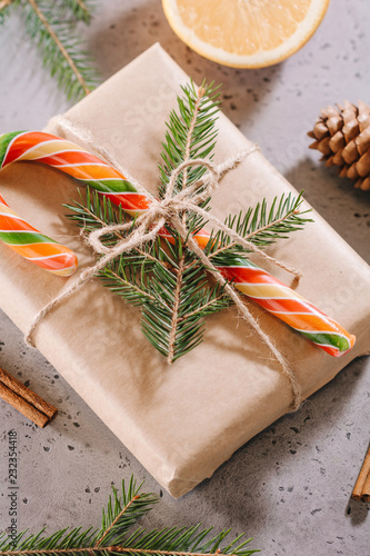 Gift box wrapped by craft paper and decorated fir branch and candy cane among winter decor on a table. The concept of Christmas presents and winter Holidays.