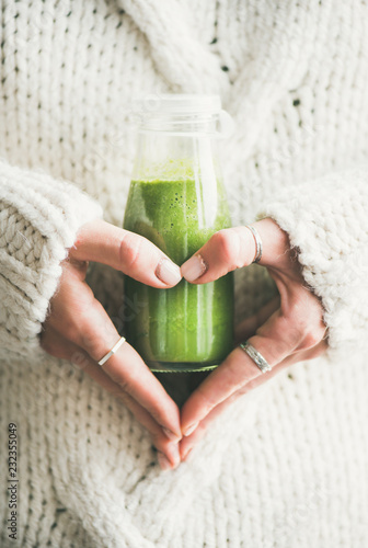 Winter seasonal smoothie drink detox. Female in knitted sweater holding bottle of green smoothie or juice making heart shape with her hands. Clean eating, weight loss, healthy dieting food concept