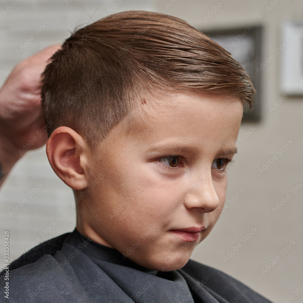 Fototapeta premium Cheerful Caucasian boy getting hairstyle in barbershop.
