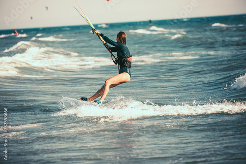 Kite surfing girl in sexy swimsuit with kite in blue sea riding waves with water splash.