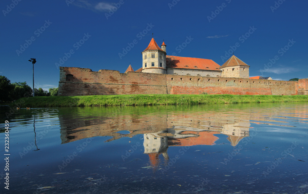 Fagaras fortress with its red stone walls under the deep blue sky mirrored in