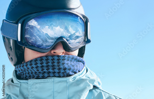 Close up of the ski goggles of a man with the reflection of snowed mountains. A mountain range reflected in the ski mask. Portrait of man at the ski resort. Wearing ski glasses. Winter Sports.