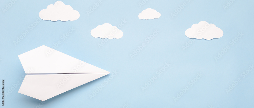 Obraz premium Flying paper plane in the clouds on a blue background. Concept of flight, travel, transfer. Top view, copy space, flat lay, banner