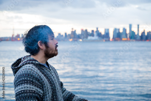 A young man smoking a joint with downtown Vancouver, BC, in the background shortly after Canadian marijuana legalization.