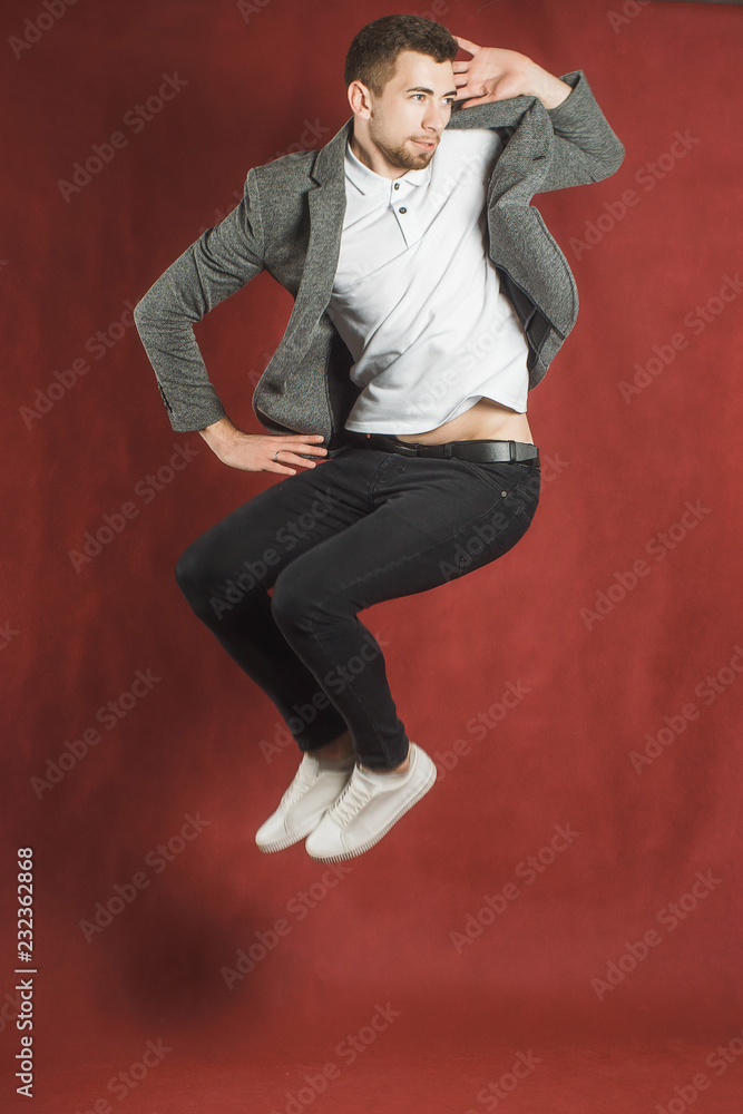 Photo of a young man on a red wall background looking at camera jumping.