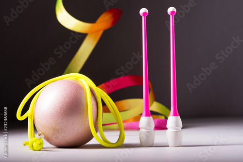 Accessories for rhythmic gymnastics ball, clubs, ribbon, rope lie on the floor. Black background