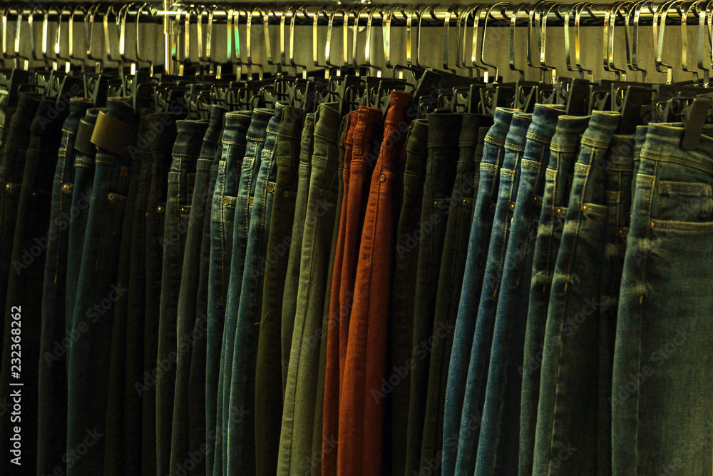 Jeans of different colors on hangers in a clothing store. Tinted in a yellow dark key. Background for design on the theme of fashion or second hand. The concept of shopping and sales.