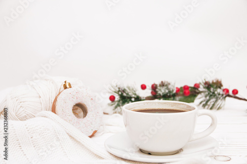 a Cup of coffee and Christmas decorations in the form of a donut on a white wooden background thread for knitting and a sprig of spruce decorated with berries