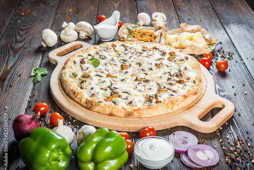Big pizza with wild mushrooms and cheese on a round cutting board on a dark wooden background. Ingredients.