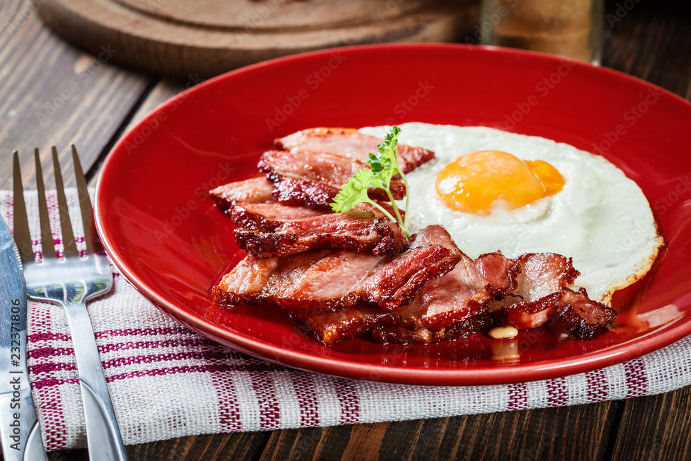 Slices of smoked bacon and fried egg on a red plate Slices of smoked bacon and fried egg on a red plate