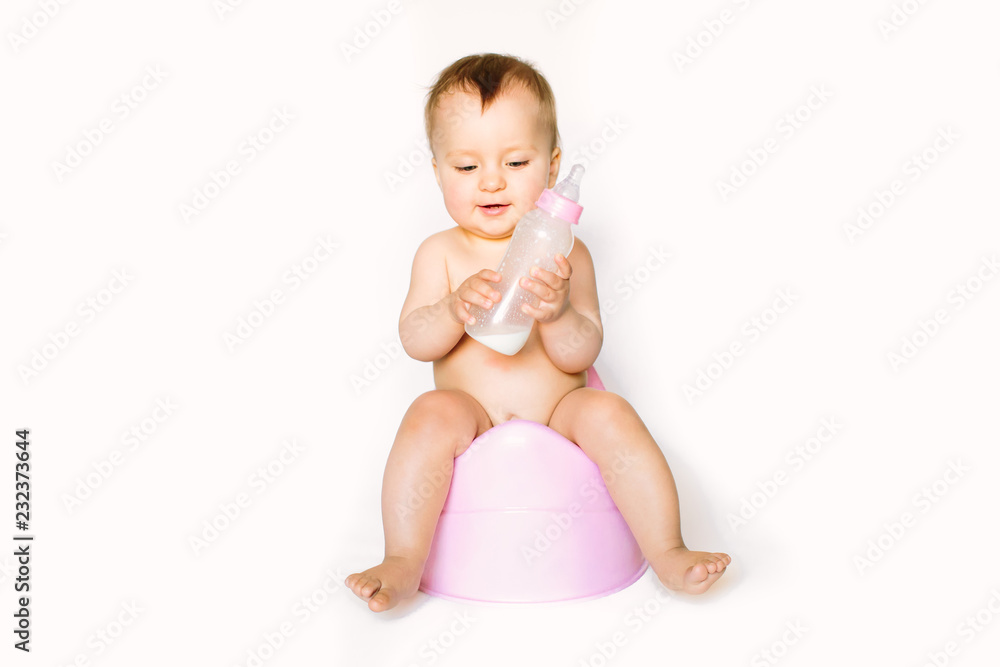Charming photo of cute baby girl holding a boottle with baby milk and sitting on a pink potty. Isolated on white background Charming photo of cute baby girl holding a boottle with baby milk and sitting on a pink potty. Isolated on white background