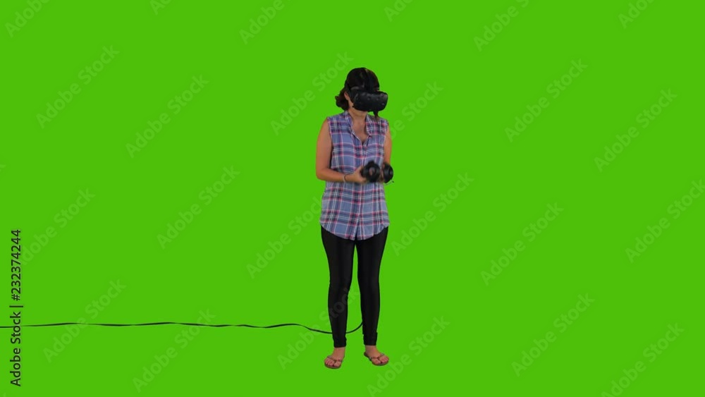 Playing a video game in a VR by a young woman over a green screen, laughing, using remotes, casual look Playing a video game in a VR by a young woman over a green screen, laughing, using remotes, casual look