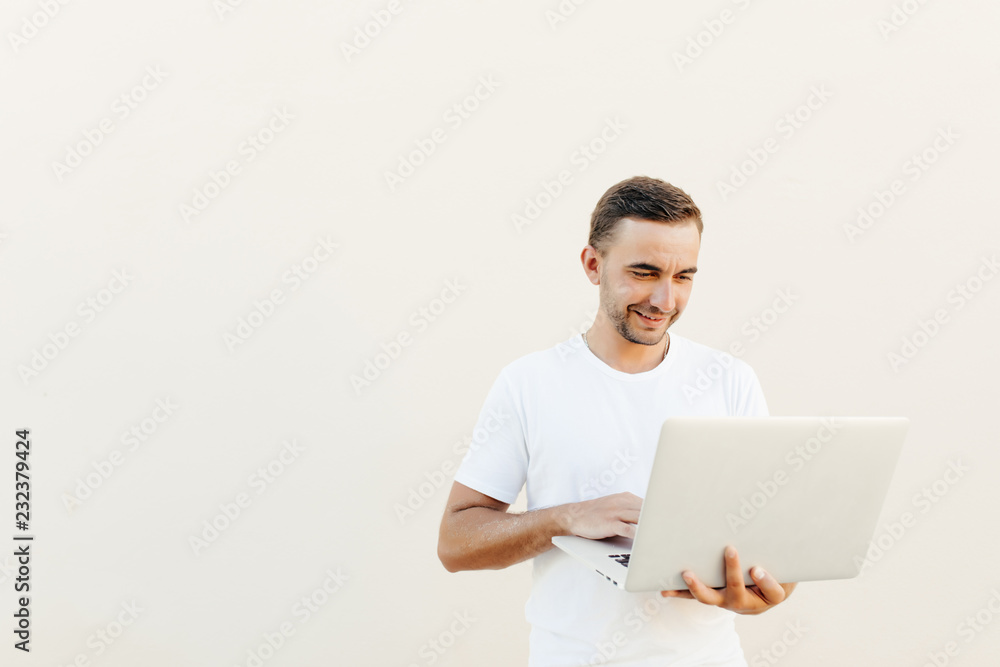 Confident young handsome man in casual clothes holding laptop and smiling while standing against orange light background Confident young handsome man in casual clothes holding laptop and smiling while standing against orange light background
