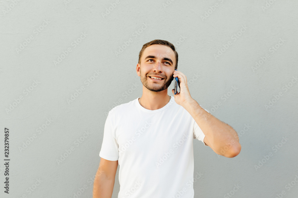 Smiling man talking by smartphone while holding his head and looking at the camera over grey background Smiling man talking by smartphone while holding his head and looking at the camera over grey background