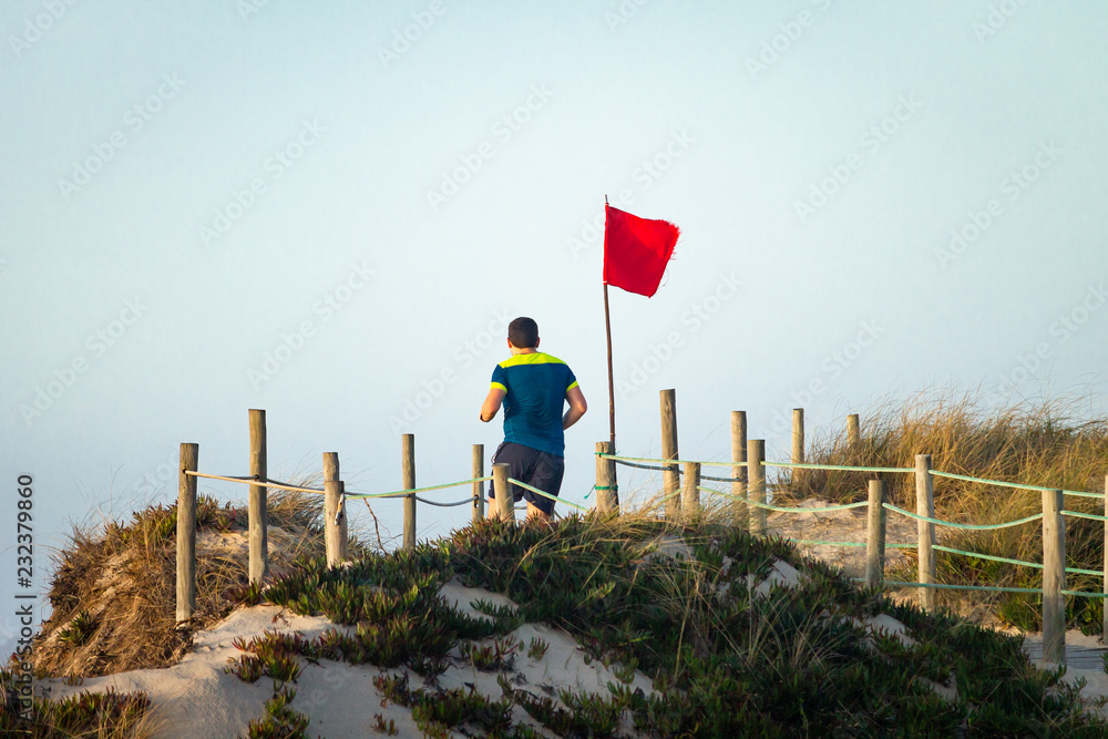 Obraz premium Male Runner Passes By Red Flag on Boardwalk