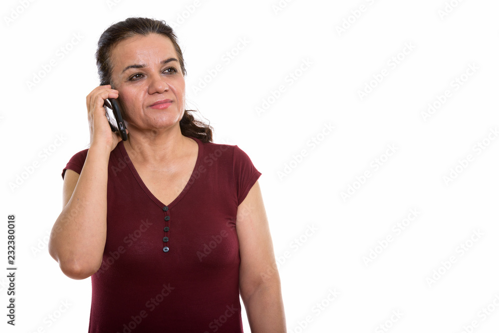 Studio shot of mature Persian woman thinking while talking on mo Studio shot of mature Persian woman thinking while talking on mo