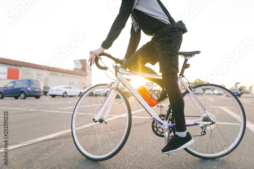 Portrait of an attractive cyclist in motion. Young rider in dark bike wears a bike on a street background and sunshine in the sunset. Transport and people.Cycling as a hobby