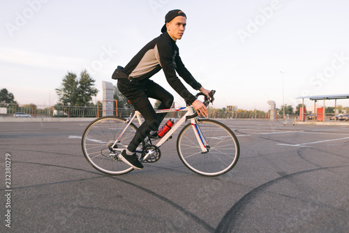 Young cyclist rides in a car parking lot for a bike. Rider wears a bike in dark sportswear