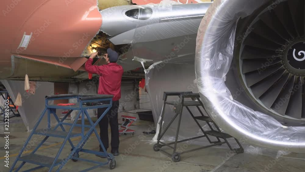 The engineer repairing the aircraft at the factory. Repair of an aircraft wing. Inspection of the fuselage. Passenger plane in the hangar in the repair. Aviation. 4K The engineer repairing the aircraft at the factory. Repair of an aircraft wing. Inspection of the fuselage. Passenger plane in the hangar in the repair. Aviation. 4K