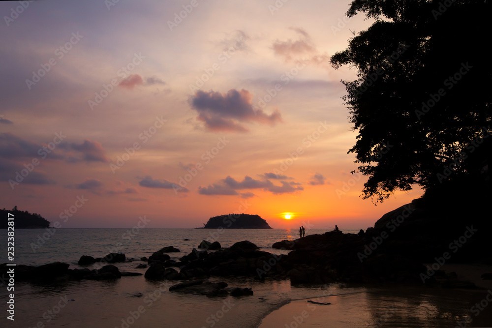 Trees and island silhouettes on tropical beach at vivid sunset time