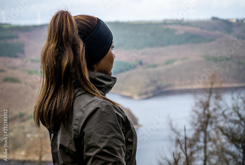 Fotografia Young beautiful female model in hike clothes wearing a headband and pigtail shot separated in front of a nature scenery in the German Eifel region