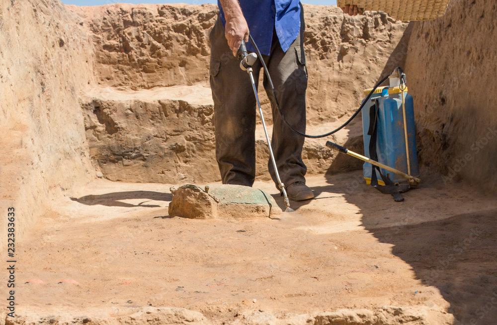 Specialized worker sprays an half-buried bronze piece at archaeological site Specialized worker sprays an half-buried bronze piece at archaeological site