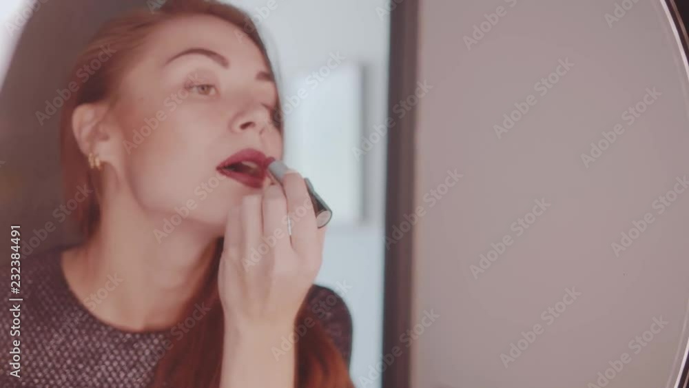 Beautiful red hair girl in elegant dress looking into a mirror and applying lipstick on her lips before party - video in slow motion Beautiful red hair girl in elegant dress looking into a mirror and applying lipstick on her lips before party - video in slow motion