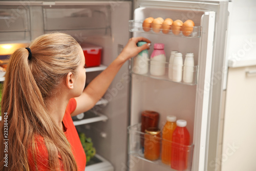Young woman taking yogurt from refrigerator at home