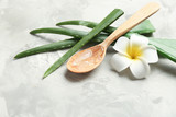 Slices of aloe vera, wooden spoon and flower on gray table