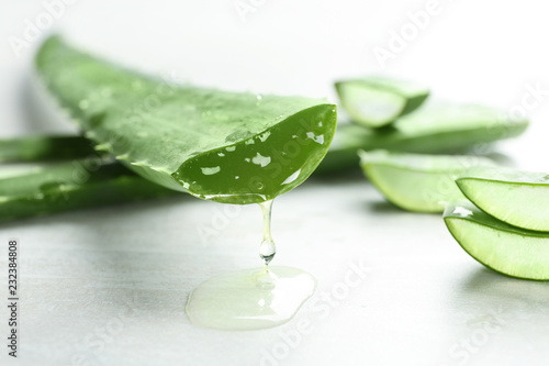Fresh sliced aloe vera leaf with dripping juice on light table, closeup