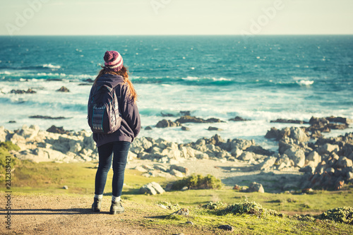Mujer exploradora parada frente al mar sobre una colina