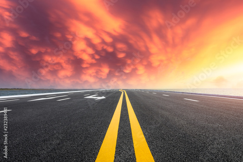 Asphalt road and dramatic sky with coastline at sunset