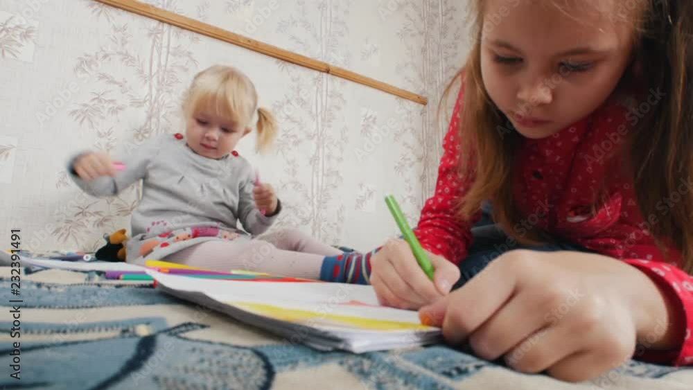 Two little girls lying on the bed and drawing Two little girls lying on the bed and drawing