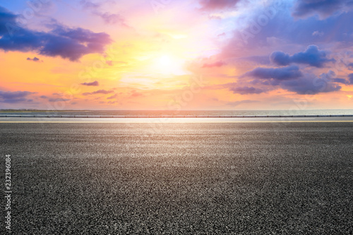 Asphalt road and dramatic sky with coastline at sunset