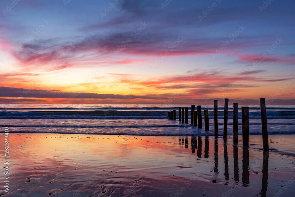 A beautiful sunset with cloud reflections at moana beach with the wooden posts seperating the beach in South Australia on 8th November 2018
