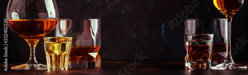Set of strong alcoholic drinks in glasses and shot glass in assortent: vodka, rum, cognac, tequila, brandy and whiskey. Dark vintage background, banner, selective focus