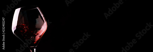 Fotografie Red wine, splash in a glass, dry cabernet sauvignon, dark background, defocused