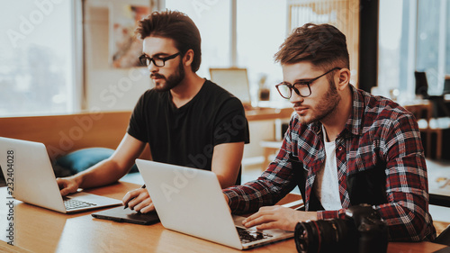 Two Photographers Fosuced on Work Using Laptop photo