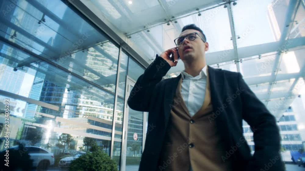 Executive is talking on the phone while having a walk next to an office building. Executive is talking on the phone while having a walk next to an office building.