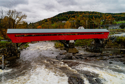 A red covered bridge first built in 1883 spans a rapidly flowing river