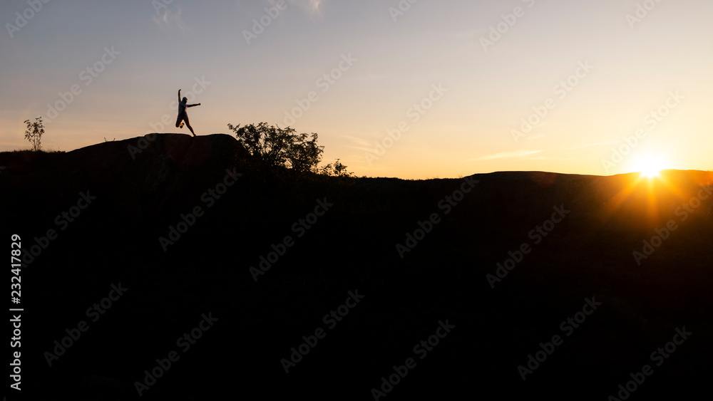 Silhouette of girl jumping against sunset with blue sky