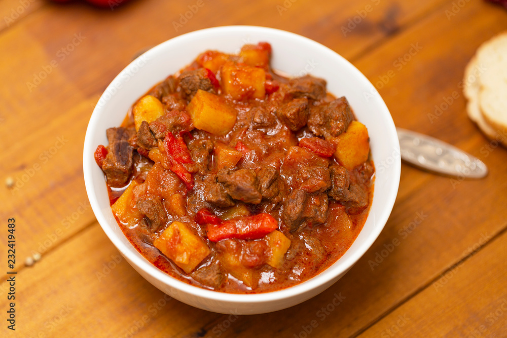Meat stew with beef, potato, carrot, onion, spices,tomato and pepper . Slow cooked meat stew, bowl, wooden background. Hot autumn-winter dish. Close up. Meat stew with beef, potato, carrot, onion, spices,tomato and pepper . Slow cooked meat stew, bowl, wooden background. Hot autumn-winter dish. Close up.