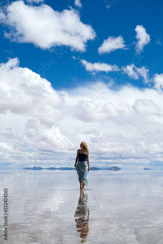 Bolivia. Salt Lake Uyuni. A blonde girl walks back in the water in a long skirt, the sky hops in the water, a natural Mirror. Clear day