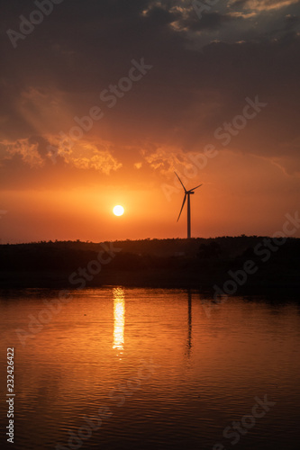 Wind turbine getting reflected in lake during sunset