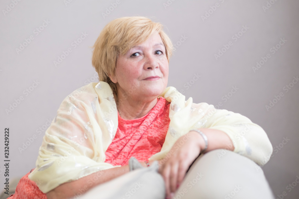 Active beautiful middle-aged woman smiling friendly and looking in camera in living room. Woman's face closeup. Realistic images without retouching with their own imperfections. Selective focus. Active beautiful middle-aged woman smiling friendly and looking in camera in living room. Woman's face closeup. Realistic images without retouching with their own imperfections. Selective focus.