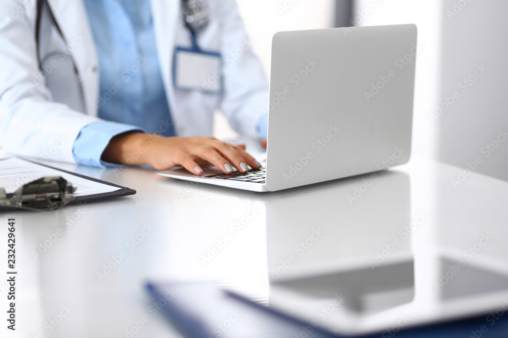 Unknown doctor woman typing on laptop computer while sitting at the desk in hospital office. close-up of hands. Physician at work. Medicine and health care concept Unknown doctor woman typing on laptop computer while sitting at the desk in hospital office. close-up of hands. Physician at work. Medicine and health care concept
