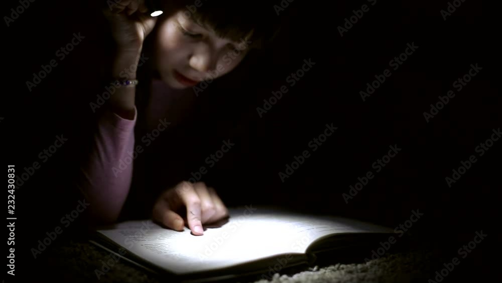 little girl is reading a book with a flashlight in a dark room at night little girl is reading a book with a flashlight in a dark room at night