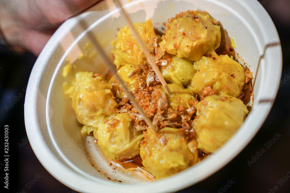 A yellow steamed dumpling topping with fried garlic put in the paper cup. At Bangkok Thailand foodstruck streetfood. A yellow steamed dumpling topping with fried garlic put in the paper cup. At Bangkok Thailand foodstruck streetfood.